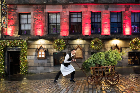 Man pushing wooden cart with a Christmas Tree outside The Witchery